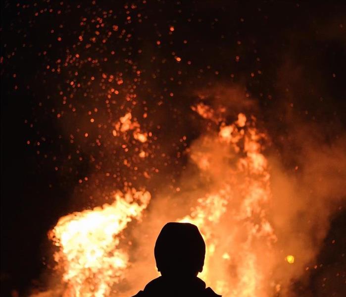 A large house fire in front of a silhouetted man.